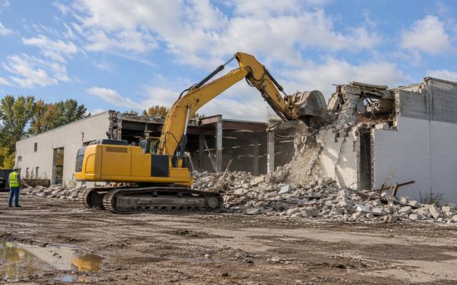 Excavator taking down a vacant single-story masonry warehouse